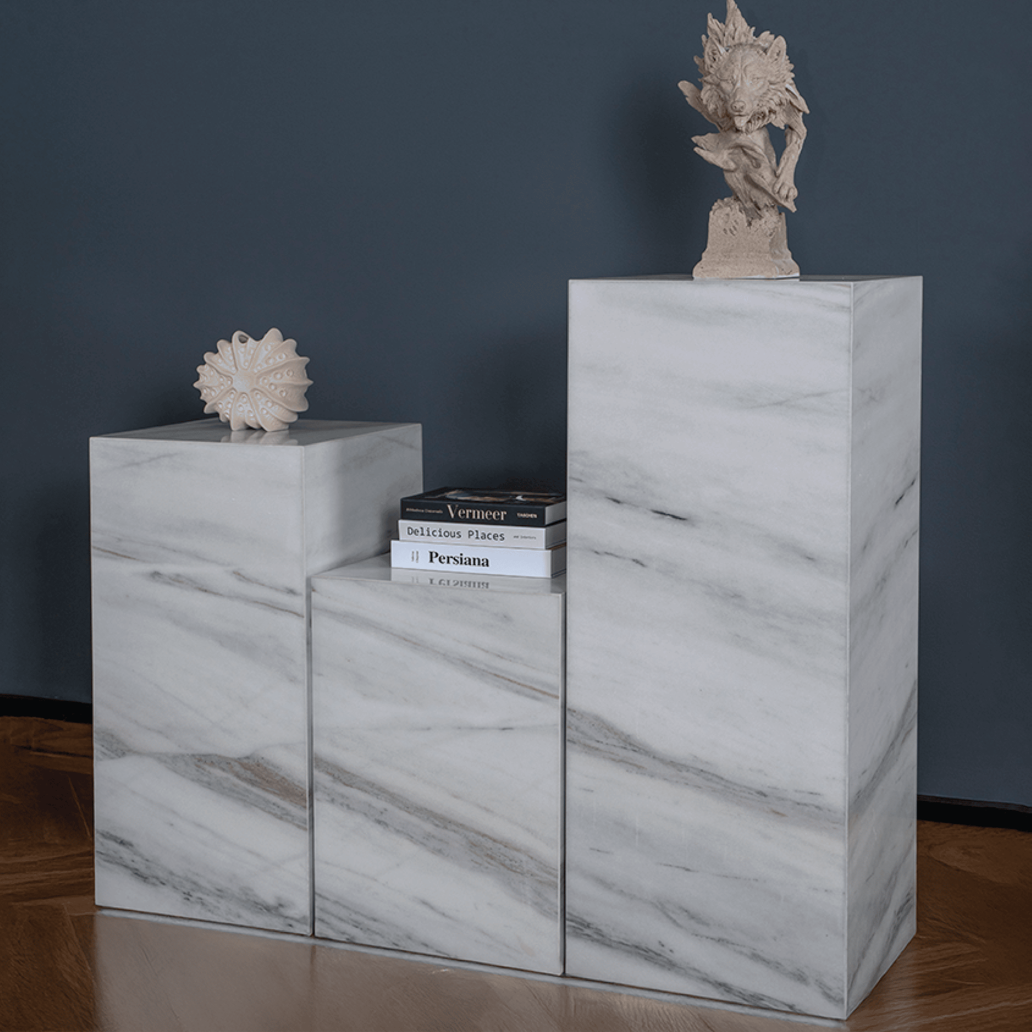 Three marble plinths with decorative items against a dark wall.
